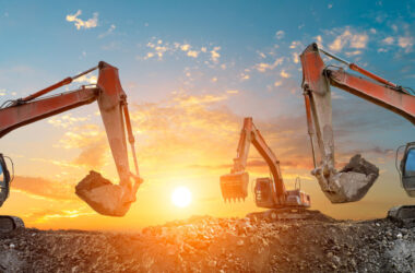 Three excavators work on construction site at sunset
