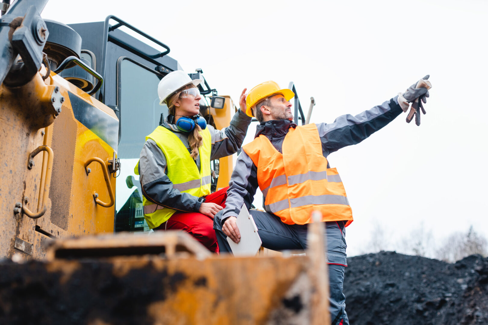 Man and woman as workers on excavator in quarry pointing at things