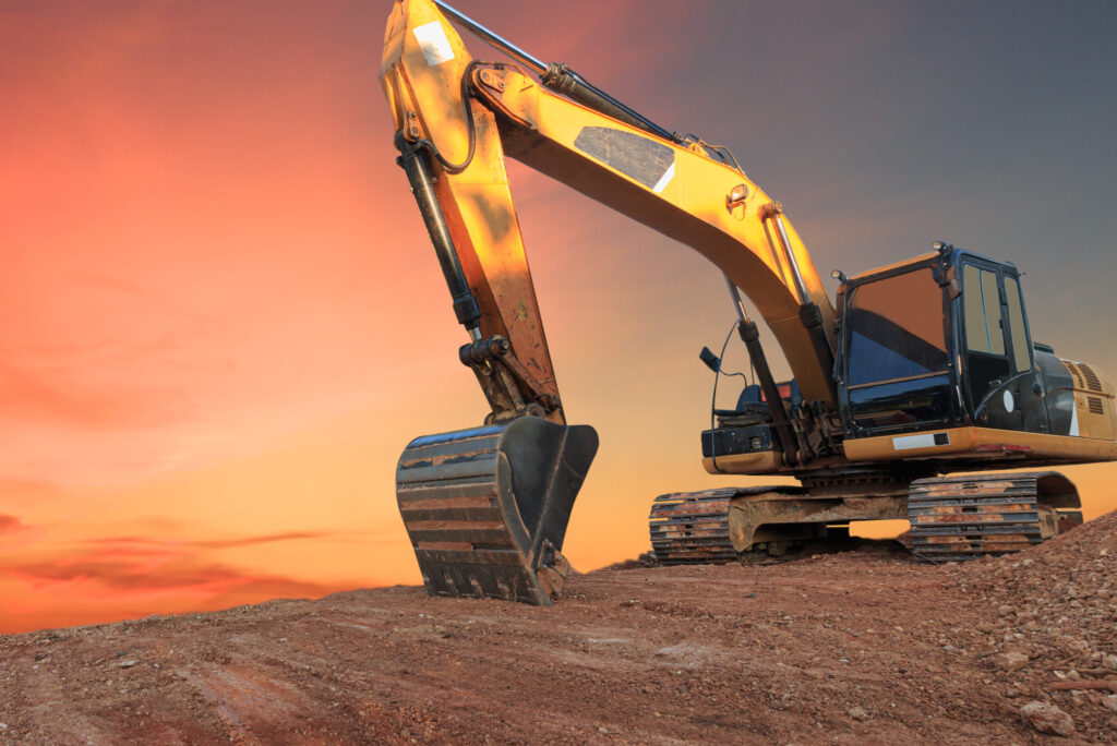 Yellow Excavators are digging the soil in the construction site on the orange sky background