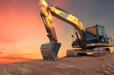Yellow Excavators are digging the soil in the construction site on the orange sky background