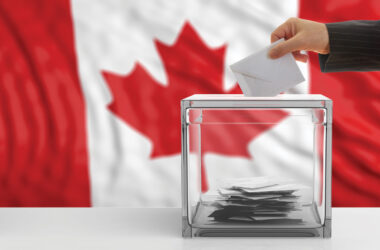 Ballot being placed in ballot box, with Canadian flag in background