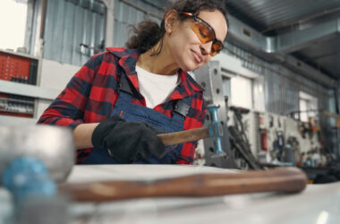 Woman with safety goggles holding hammer at work bench