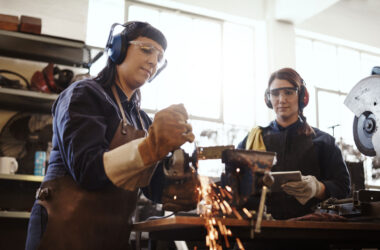 Two young female artisans using an angle grinder in their workshop.