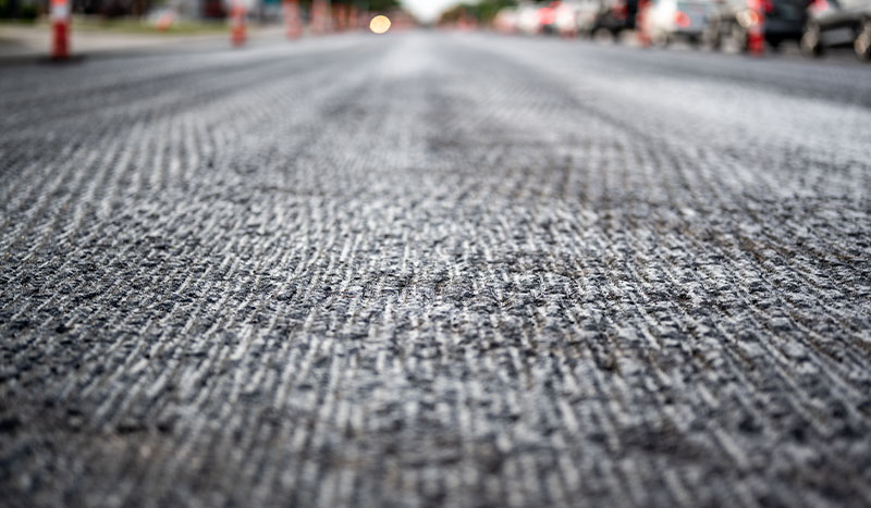 A close-up view of a freshly paved road, showcasing the intricate texture and layers of asphalt, hinting at the ongoing urban development and infrastructure improvements in the area.