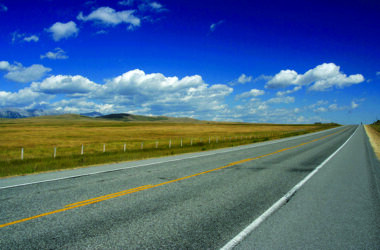 Straight prairie road in Alberta, Canada. Yellow line. Blue sky.