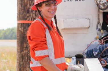 A photo of a girl in a construction uniform and wearing an orange hard hat.