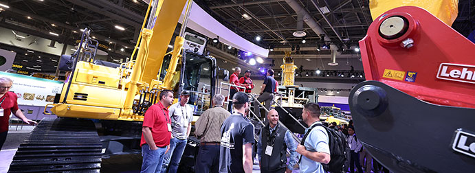 People talking in a conference event, in front of a backhoe machine.