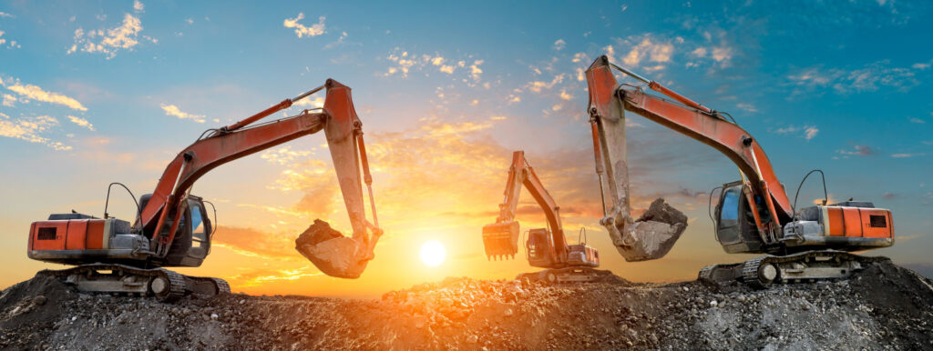 Three excavators work on construction site at sunset