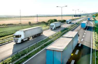 Transportation trucks in line passing on a highway on a bright blue day. Highway transit transportation with lorry trucks. Transportation And Trucking Industry.