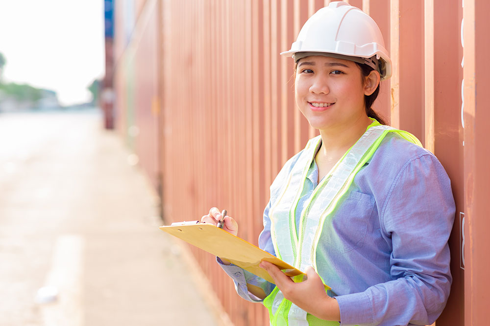 Asian young teen happy worker checking stock in shipping port work manage import export cargo containers.