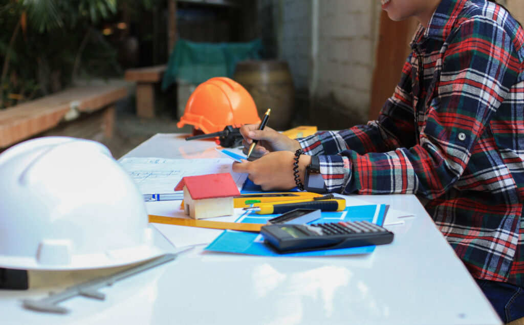 Person sitting at desk cluttered with hard hats and drafting tools