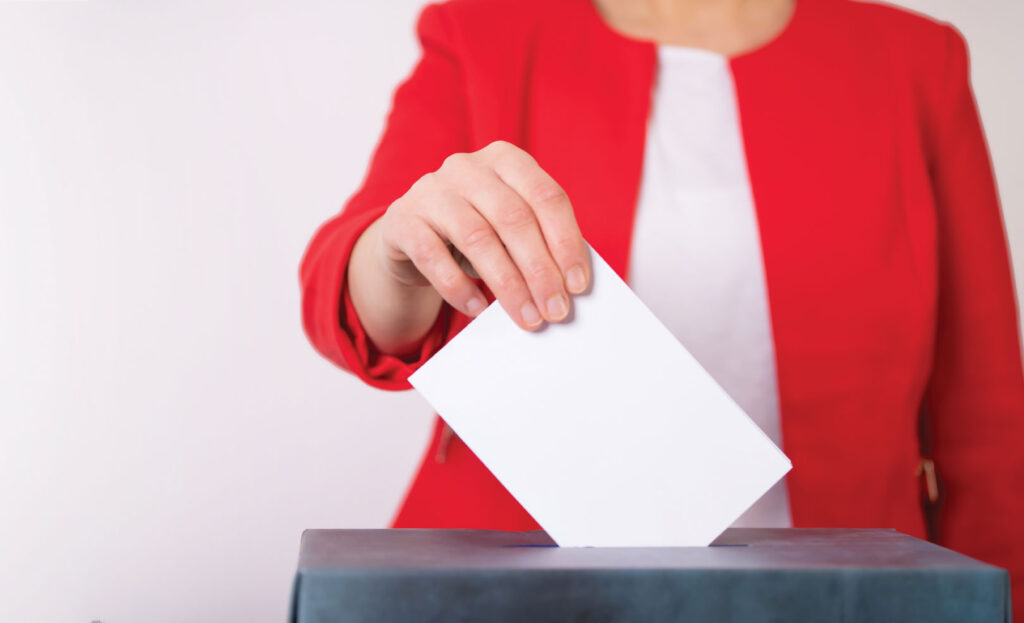 Lady in red jacket dropping ballot in box