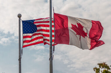 American and Canadian Flags Against Bright Skies