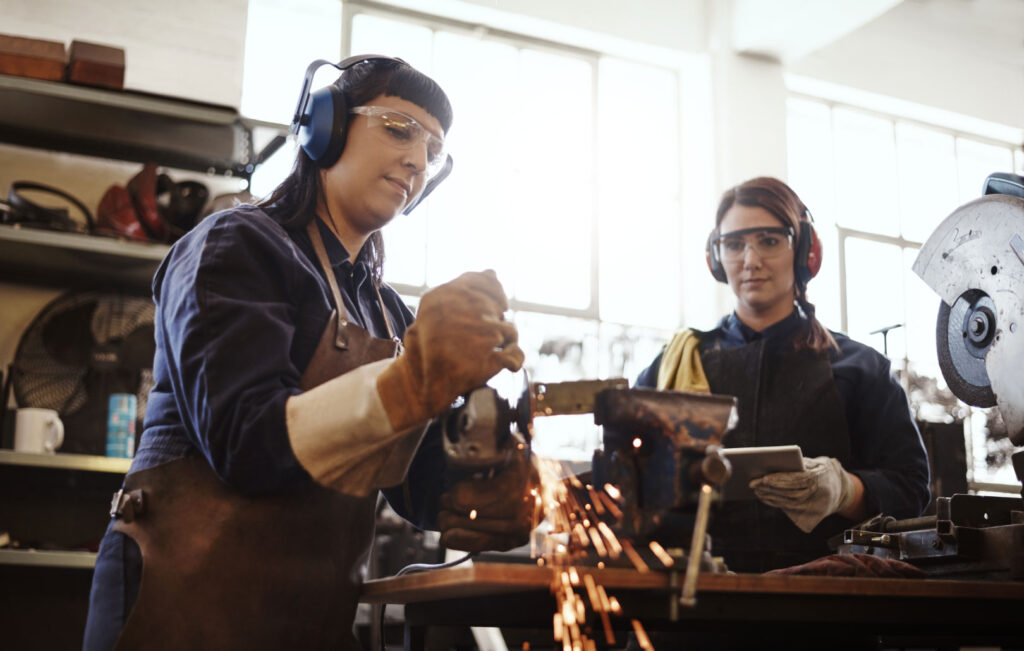 Two young female artisans using an angle grinder in their workshop.