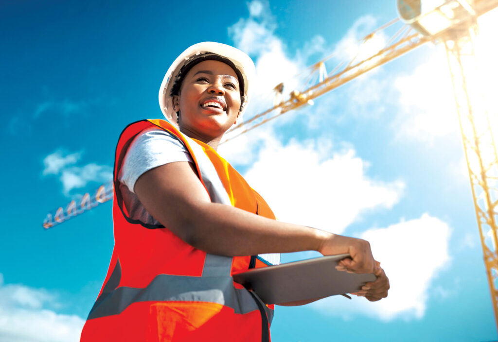 Woman holding clipboard wearing hardhat and safety vest on job site