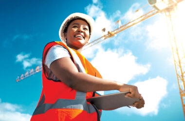 Woman holding clipboard wearing hardhat and safety vest on job site