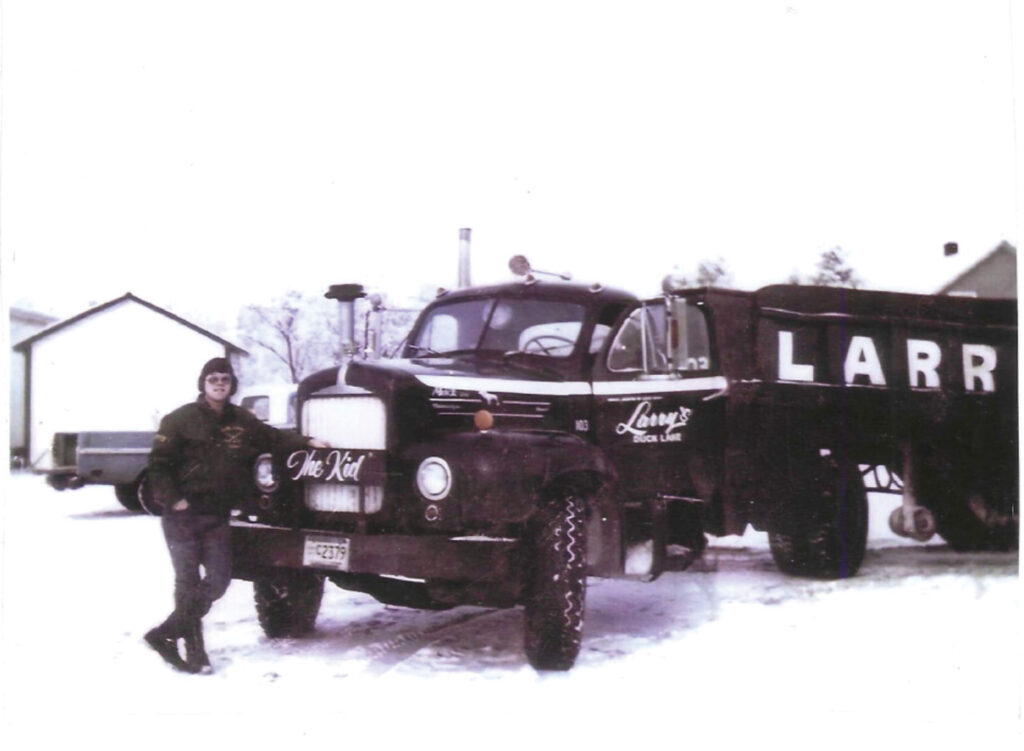 Black and white photo of Larry Urick leaning against truck in winter