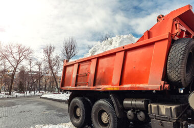 Tractor loader machine uploading dirty snow into dump truck. Cleaning city street, removing snow and ice after heavy snowfalls and blizzard. Snowplow outdoors clean pavement sidewalk road driveway