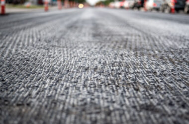 A close-up view of a freshly paved road, showcasing the intricate texture and layers of asphalt, hinting at the ongoing urban development and infrastructure improvements in the area.