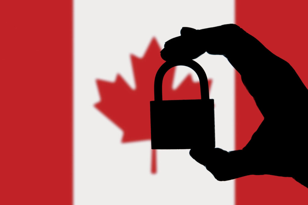 Silhouette of hand holding a padlock with Canadian flag in background