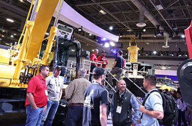 People talking in a conference event, in front of a backhoe machine.