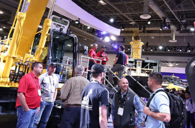 People talking in a conference event in front of a backhoe machine.