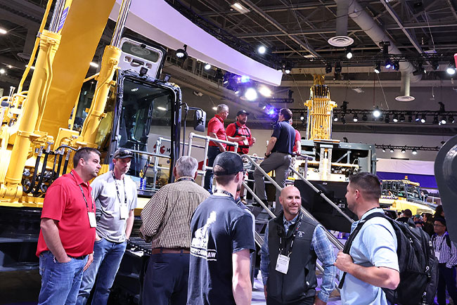 People talking in a conference event in front of a backhoe machine.