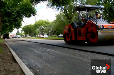A screenshot of a global news video that shows a compactor flattening the asphalt.