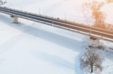Car bridge over frozen river aerial drone view.
