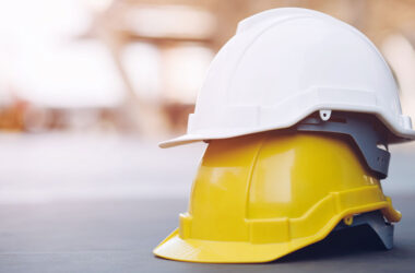 yellow and white hard safety wear helmet hat in the project at construction site building on concrete floor on city with sunlight.