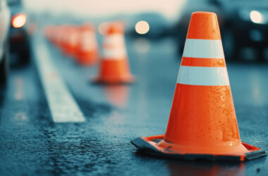 Close-up of a wet traffic cone on a road, with blurred cars in the background