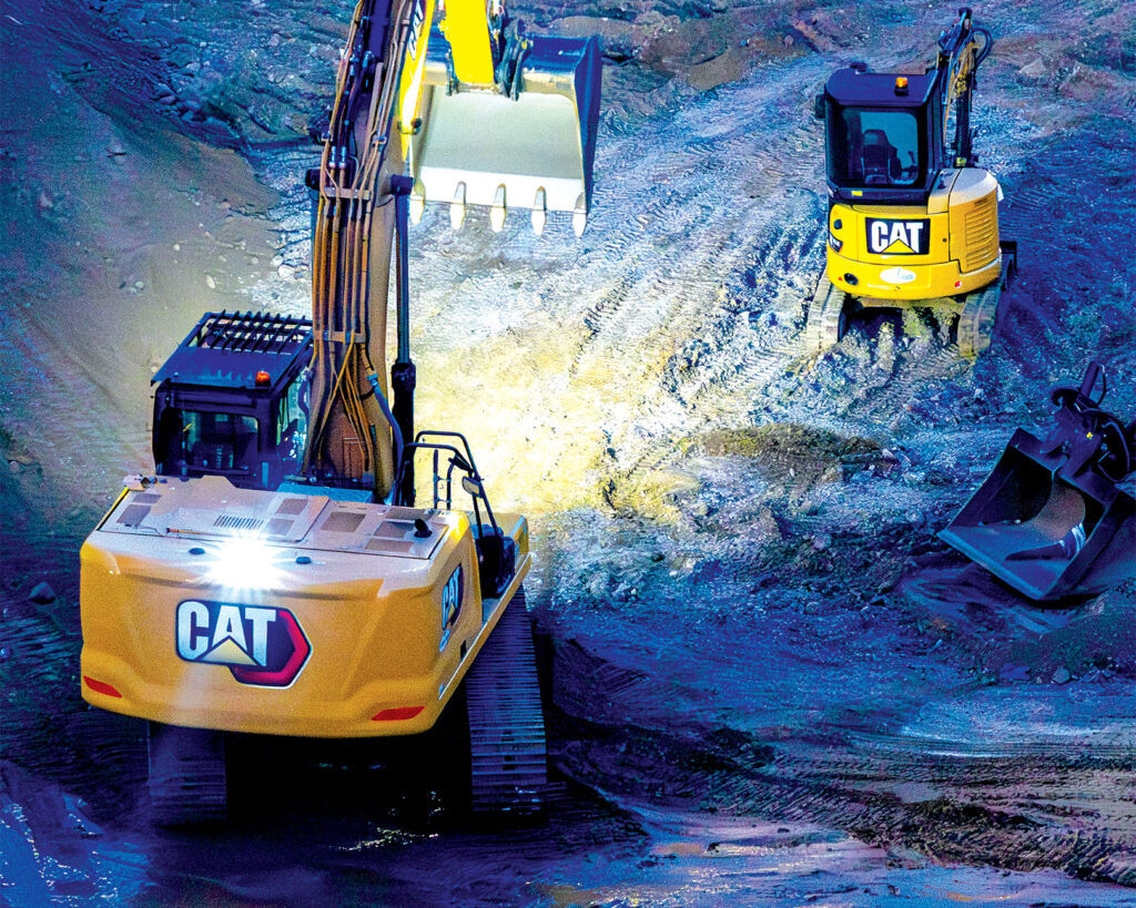 Two excavators working on a construction site at night.