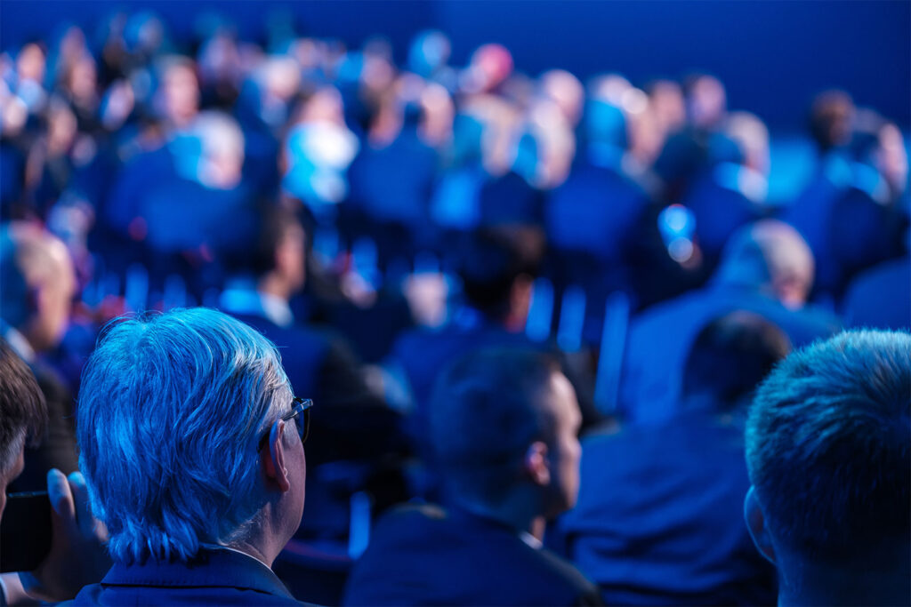 seated crowd listening to speaker giving presentation in illuminated auditorium