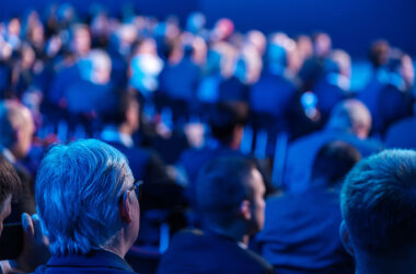 seated crowd listening to speaker giving presentation in illuminated auditorium