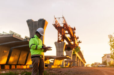 A construction worker is standing on a bridge, talking on his cell phone