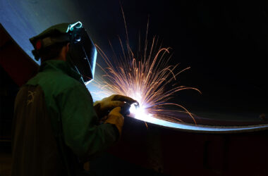 Person welding very large steel pipe with blue tones and orange sparks with nice leading pipe line