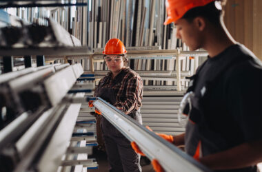 Young workers wearing hard hats and safety glasses handling window profiles