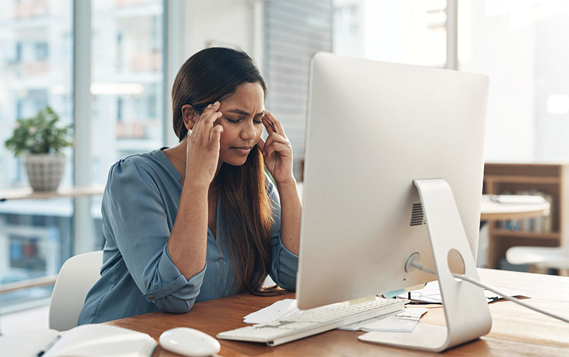 Female employee sitting at desk, rubbing temples, looking stressed